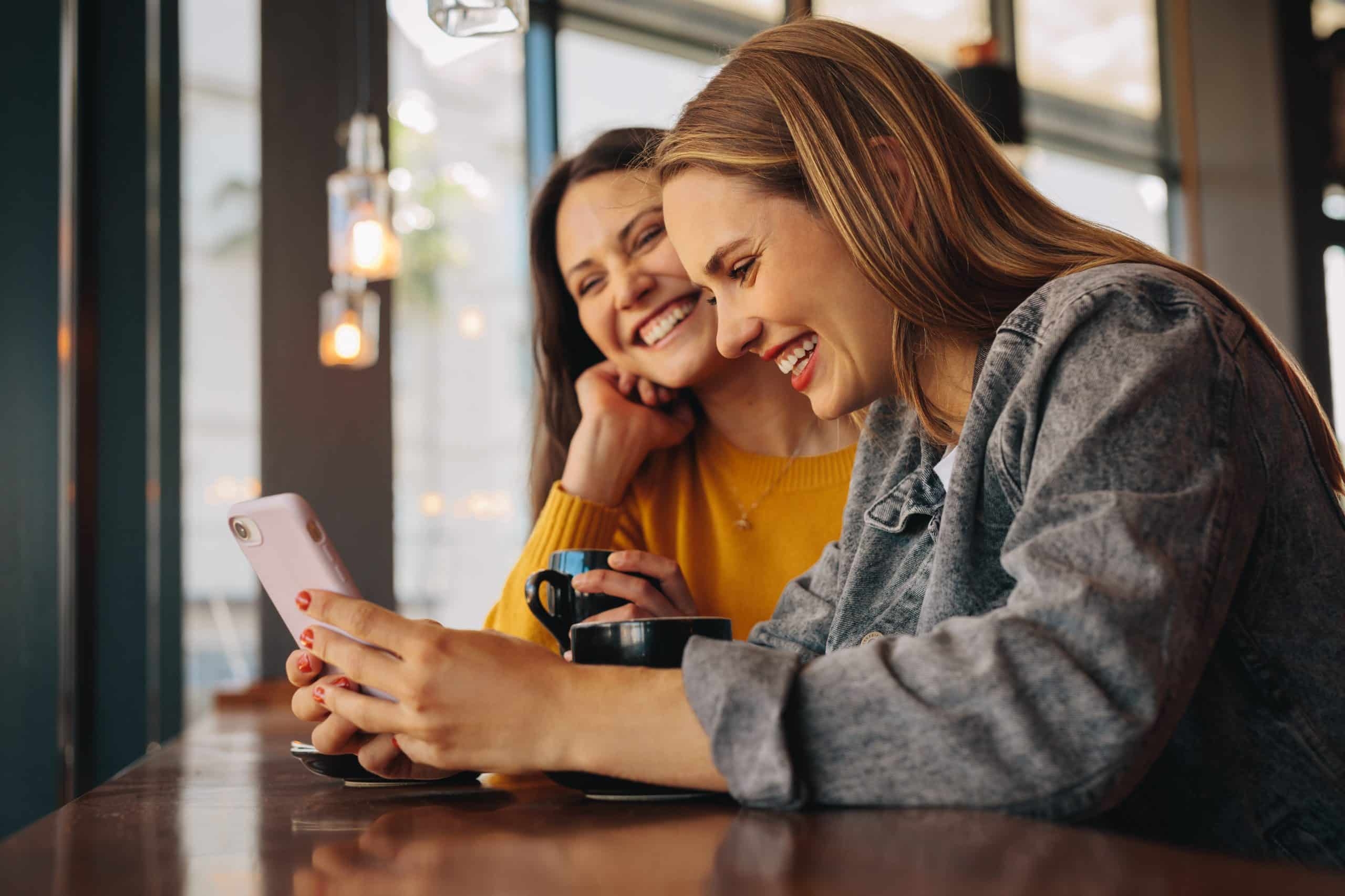 Woman taking selfie indoors, friends laughing together on couch, candid woman laughing in cafe